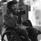 “Behind the scenes” - Camera man who uses a wheelchair is in deep concentration as he films an interview.